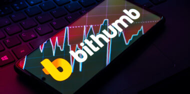 the Bithumb logo is seen displayed on a smartphone placed on top of computer keyboard