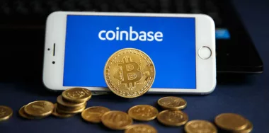 Coinbase logo displayed on smartphone screen with Bitcoin BTC on stack of cryptocurrencies