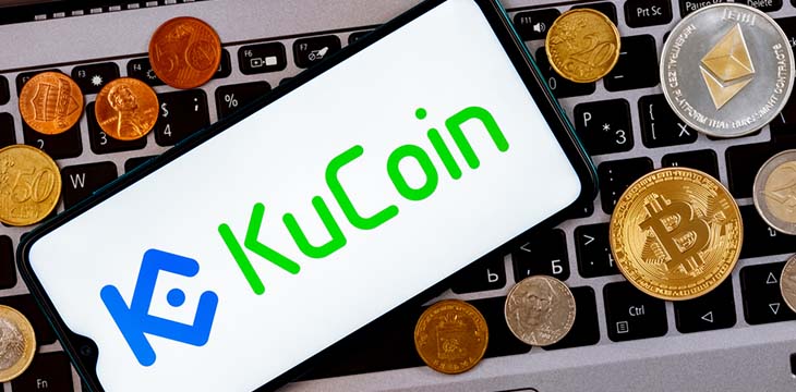 KuCoin logo on phone with crypto coins