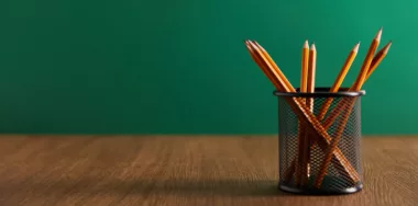 Pencils on wooden table with green chalkboard on background