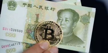 person holding a gold bitcoin and chinese yuan