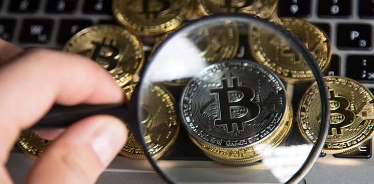 silver bitcoin under a magnifying glass with gold bitcoins