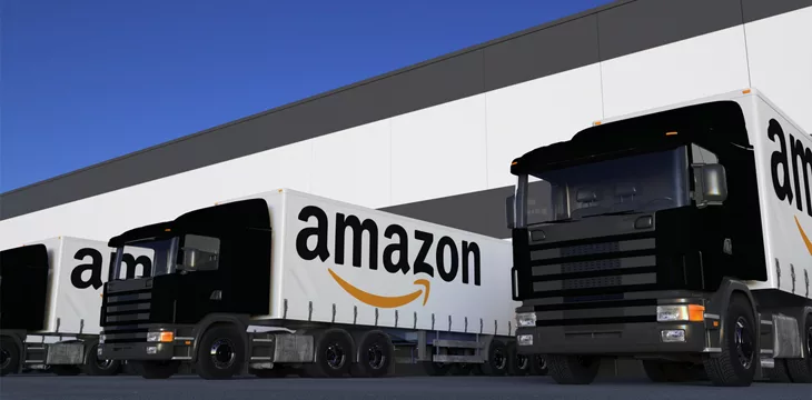 Freight semi trucks with Amazon.com logo loading or unloading at warehouse dock