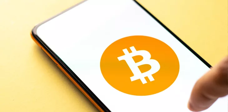 Smartphone screen showing Bitcoin logo with finger tapping on it