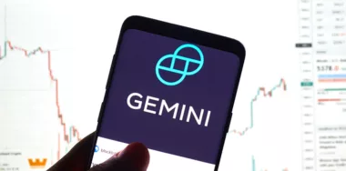 Gemini logo on smartphone with stocks on the background