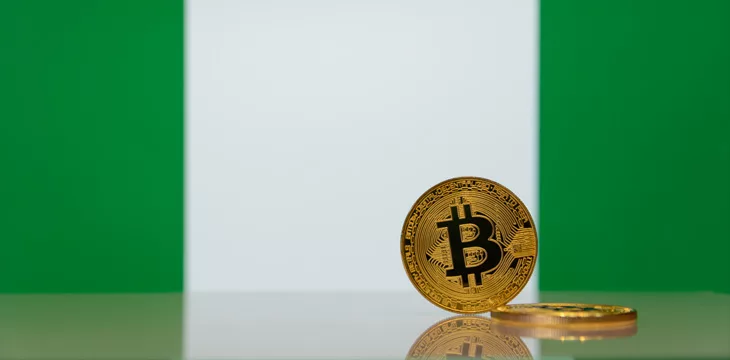 Golden bitcoin stands on a blurred background of state flag of Nigeria