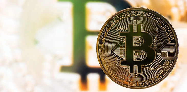Gold Bitcoin in front of a blurred golden bitcoin background