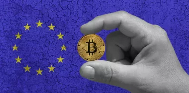 One hand hold a Bitcoin, btc, the cryptocurrency of the future. In the background the European flag on a ruined concrete wall