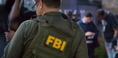Caucasian male FBI agent wearing glasses in a green bulletproof vest with FBI logo seen from behind on the investigation spot