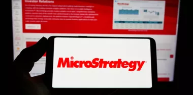 Person holding mobile phone with logo of US software company MicroStrategy Inc. on screen in front of business web page. Focus on phone display.