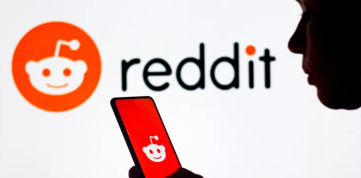 a woman's silhouette holds a smartphone with the Reddit logo displayed on the screen and in the background