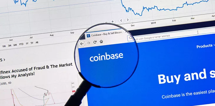 Coinbase cryptocurrency digital assets exchange logo and home page on a laptop screen under magnifying glass