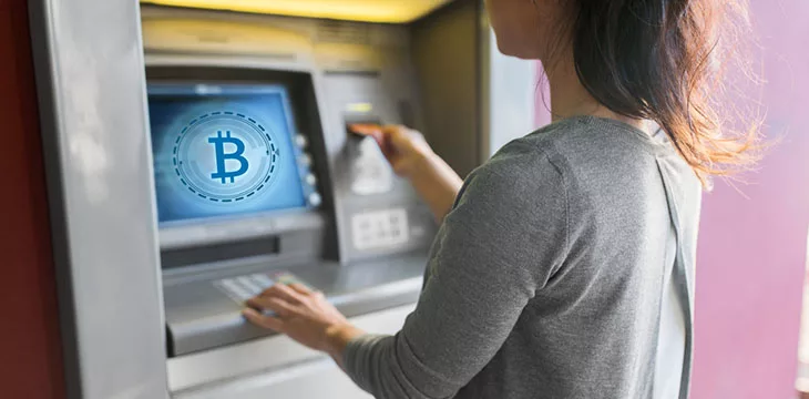 woman inserting card on atm machine with bitcoin sign on screen