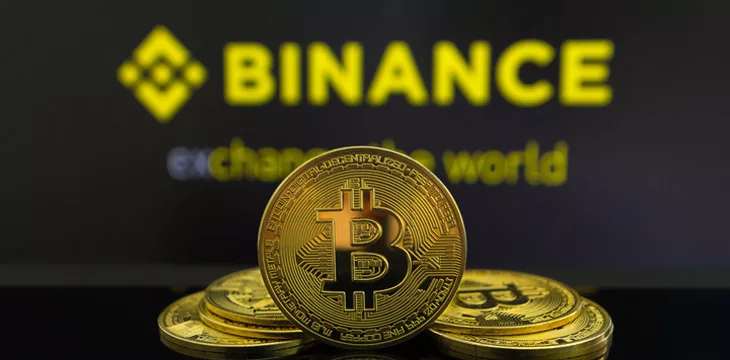A big Bitcoin cryptocurrency coin in the centre and other bitcoin coins from both side in front of Binance crypto market