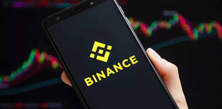 Binance logo on smartphone with stocks background