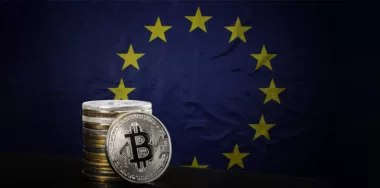EU flag with one silver bitcoin and stack of bitcoins