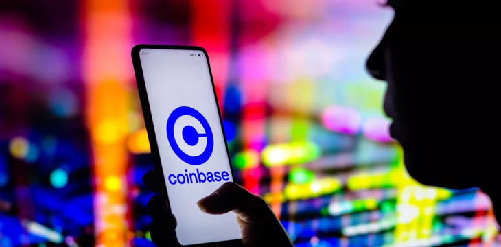 Silhouette of a person holding a smartphone displaying Coinbase logo