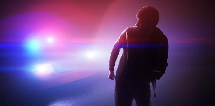 Silhouette of young man running away from a police car