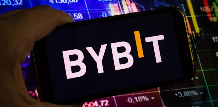 Smartphone displaying logo of Bybit cryptocurrency exchange on stock exchange diagram background