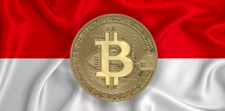 Physical golden Bitcoin laying on top of flag of Indonesia