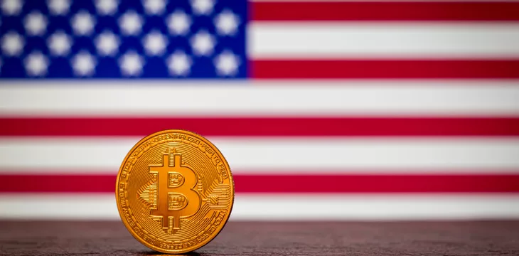 Golden physical Bitcoin with United States flag in the background