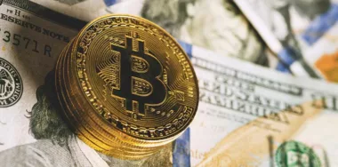 Close-up of bitcoin on benjamin franklin's face on piles of $100 bills