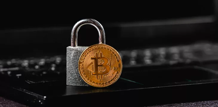 Golden bitcoin and small padlock placed on netbook keyboard as symbols of secure cryptocurrency trade