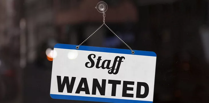Close-up on a blue open sign in the window of a shop displaying the message: Staff wanted