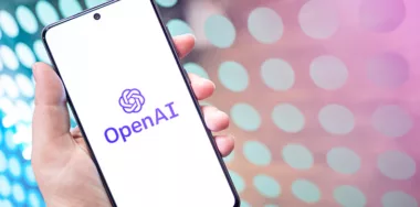 OpenAI logo displayed on the phone screen in hand, colorful neon background with copy space for text