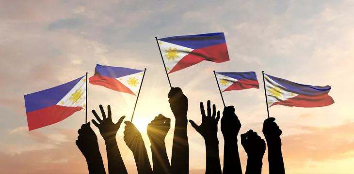 Silhouette of arms raised waving a Philippines flag with pride