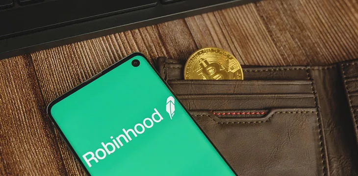 Robinhood app green logo with gold Bitcoin in a brown wallet and keyboard on wood backround