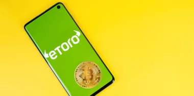 Smartphone with Etoro logo with Bitcoin coin on yellow background