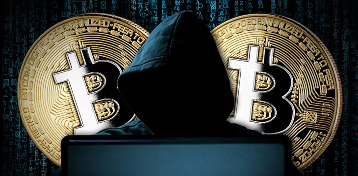 Hacker with bitcoins behind notebook laptop in front of blue source binary code background internet cyber hack attack crypto currency blockchain computer concept