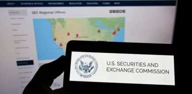 Person holding mobile phone with logo of US agency Securities and Exchange Commission on screen in front of web page. Focus on phone display