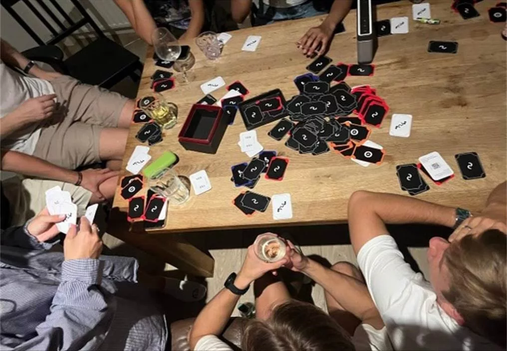 Group of people gathered around a wooden table playing Dark 2 Light card game