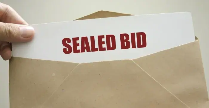 Sealed Bid text on paper being put inside brown envelope.