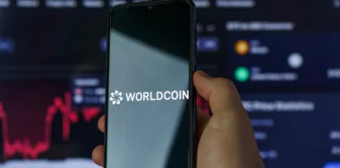 Worldcoin logo shown on smarphone screen with stock chart in the background