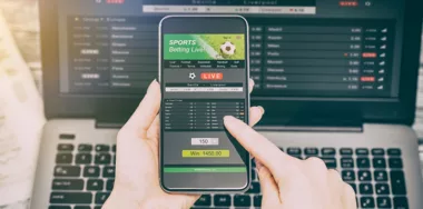 Man using smartphone and laptop with sports betting app