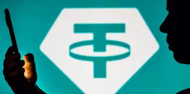 Tether logo with man holding mobile phone
