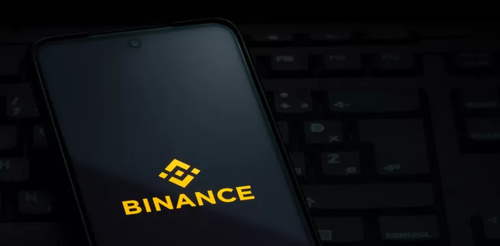 Binance exchange logo on smartphone screen laying on computer keyboard