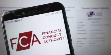 FCA Financial Conduct Authority logo displayed on mobile phone with background of FCA website displayed on desktop screen