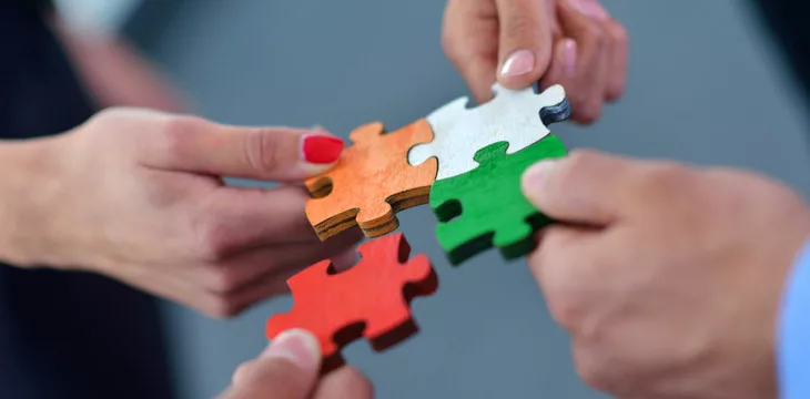 Collaboration concept image of four people putting together jigsaw puzzle pieces