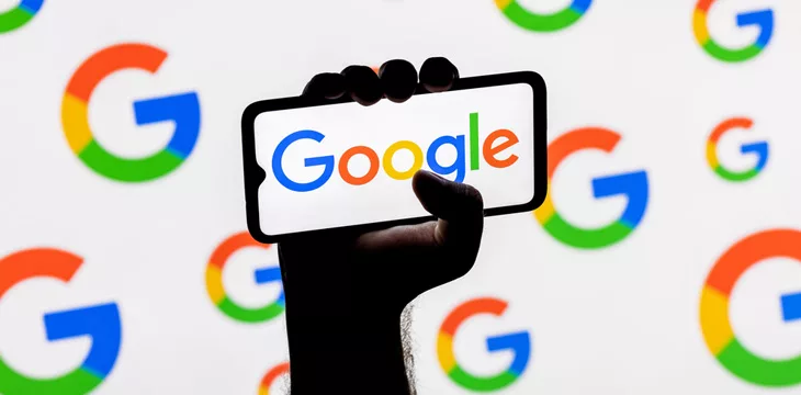 Smartphone with the Google technology company logo on the screen in a clenched hand on the background of Google logos