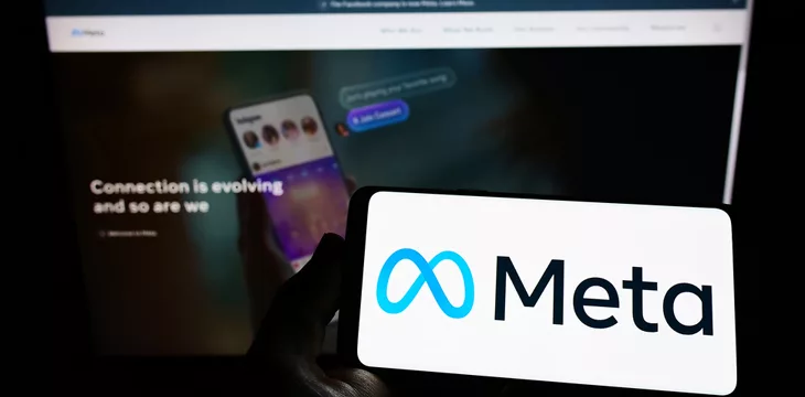 Person holding smartphone with logo of US technology company Meta Platforms Inc. (Facebook) on screen in front of website. Focus on phone display