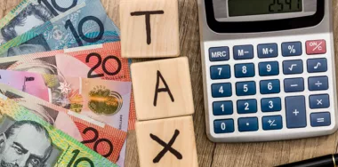 Tax word on wooden cubes with Australian bank notes, pen, and calculator