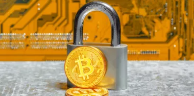 Physical verision of Bitcoin next to silver padlock with background of circuit board
