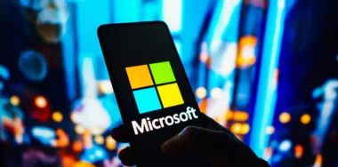 Microsoft logo displayed on smartphone screen with background of bokeh lights