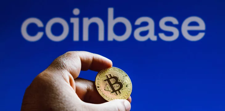 hand holding a bitcoin with coinbase logo in blue background