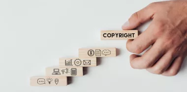 Cropped view of man holding wooden block with word 'copyright' on top of wooden bricks with icons isolated on white
