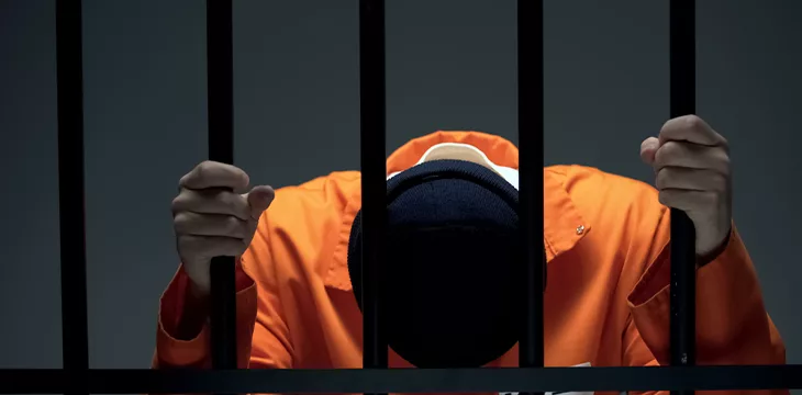 Male prisoner holding bars and leaning head, feeling depressed and guilty
